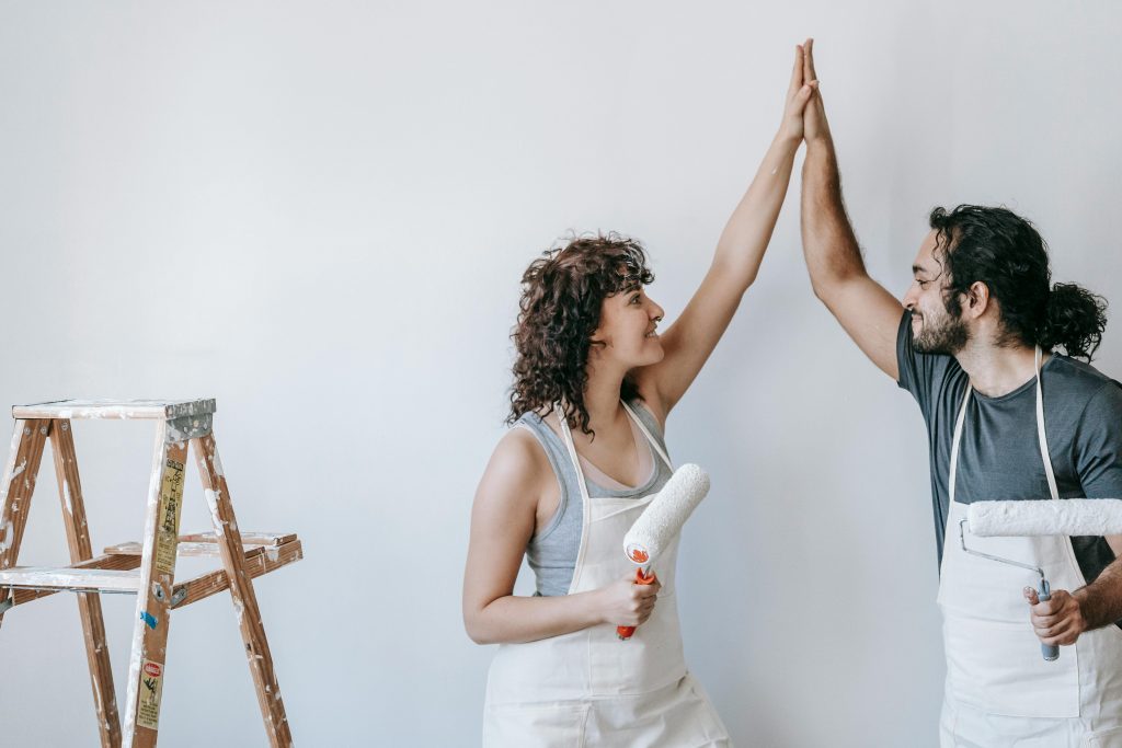 A joyful couple high-fiving during a home painting project, expressing teamwork and success.