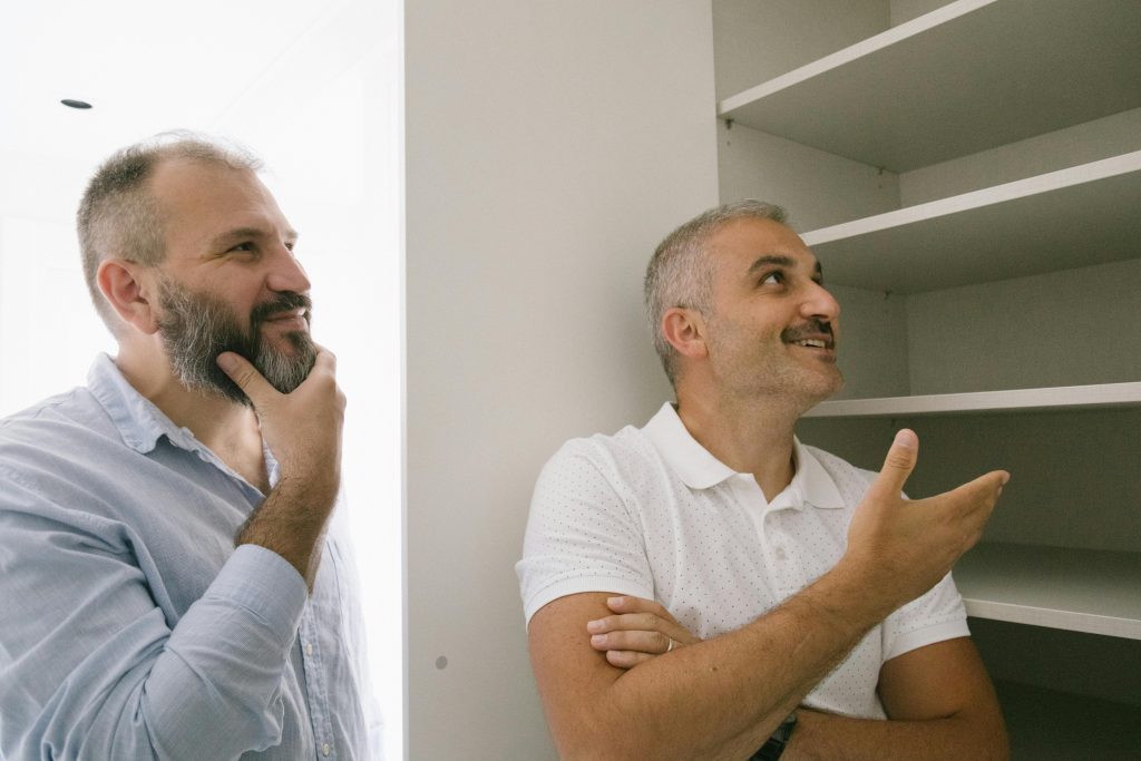 Two men engage in a conversation about a shelving unit in a bright indoor setting.